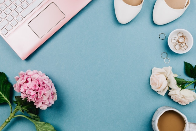 Wunderschönes feminines flatlay aus rosa laptop und weißen schuhen der frau, schmuck und blumen auf blauem, selektivem fokus