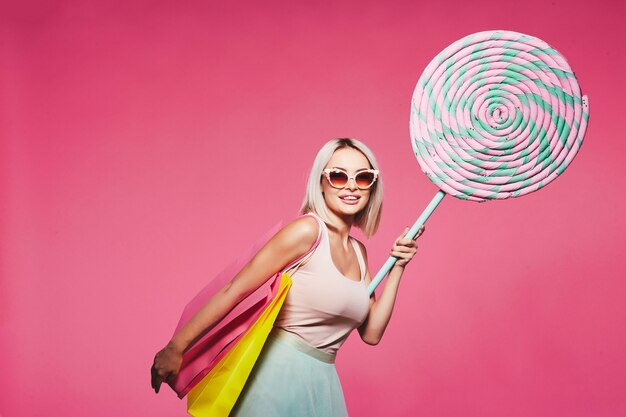 Wunderschönes Mädchen mit blonden Haaren, das Oberteil und Rock trägt und mit riesigen süßen Lutschern steht