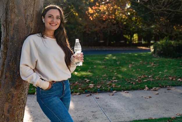 Wunderschönes Teenager-Mädchen, das am Nachmittag eine Flasche Wasser in einem Park hält
