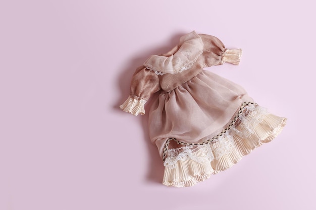 Wunderschönes Vintage-Kleid mit Rüschen für eine Puppe auf rosafarbenem Hintergrund mit Kopierraum
