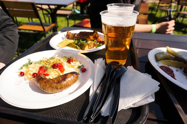 Wurst mit Salat auf einem Teller und hellem Bier auf einem Tablett Streetfood