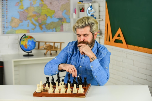 Xadrez é o ginásio da mente lição de xadrez conceito de estratégia professor de escola jogo de tabuleiro homem hipster inteligente jogando xadrez passatempo intelectual figuras no tabuleiro de xadrez de madeira pensando no próximo passo