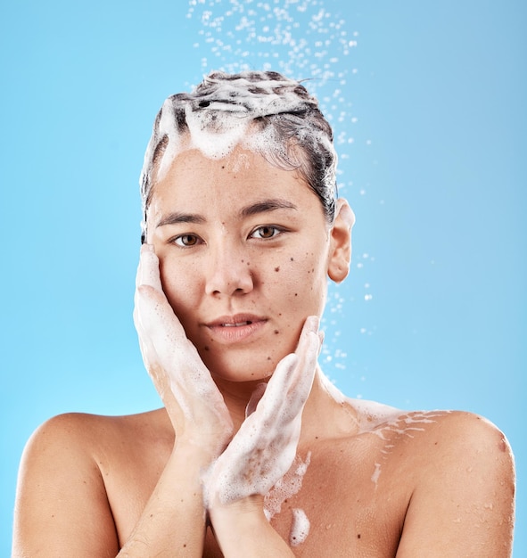 Xampu de banho e mulher de cuidados com o cabelo com sabão e retrato limpo para preparação e higiene contra o fundo azul do estúdio face mãos e bem-estar com lavagem de cabelo e beleza com gotas de água