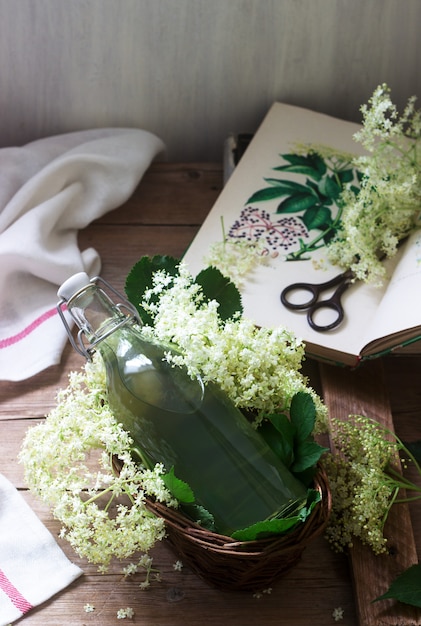 Xarope caseiro de flores de sabugueiro em uma jarra de vidro e ramos mais velhos em uma mesa de madeira estilo rústico.