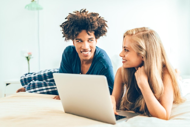 XAYoung lindo casal inter-racial relaxado deitado na cama no computador