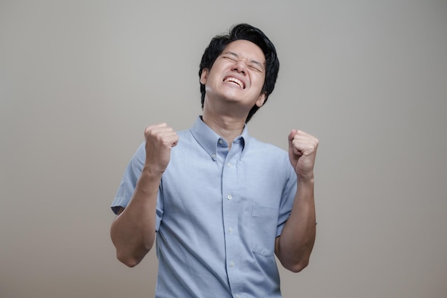 Foto xdxaerfolgreicher mann und überraschung im blauen hemd, der sich über den sieg freut, glücklich die hände hochhebt und ja-konzept, großartige neuigkeiten sagt