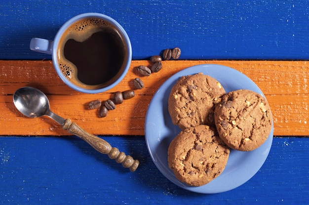 Xícara azul de café quente com saborosos biscoitos de chocolate na mesa de madeira colorida vista superior