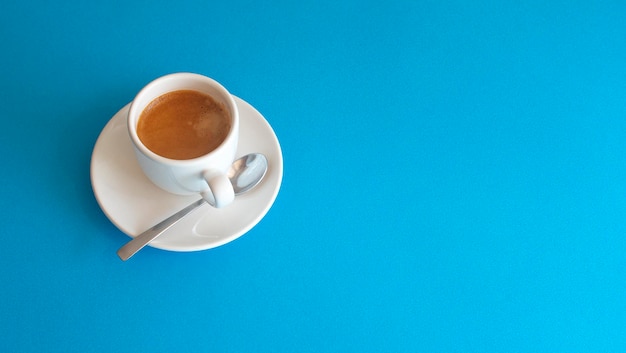 Xícara branca com café e uma colher de metal brilhante sobre fundo azul