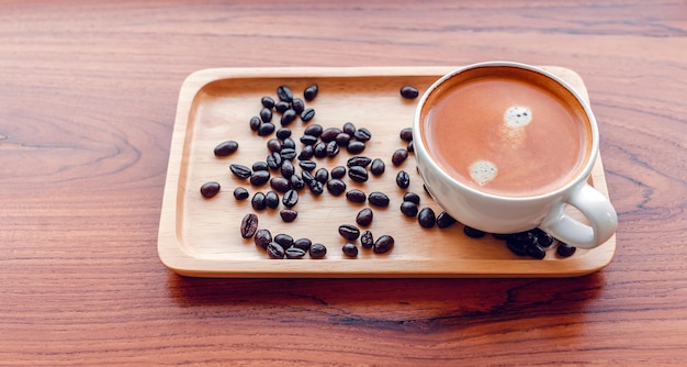 Xícara branca de café expresso e grãos de café torrados em uma bandeja de madeira