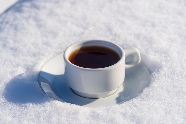 Xícara branca de café quente em uma cama de neve e fundo branco fecha