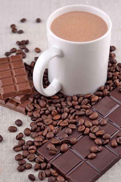 Xícara branca de chocolate quente em grãos de café e backgro de chocolate