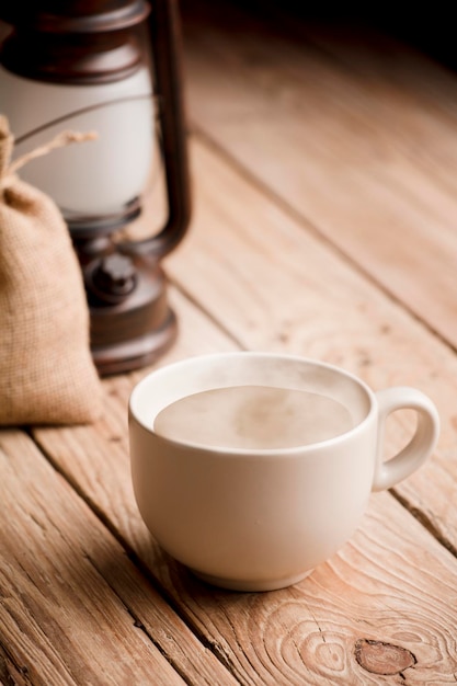 Xícara com café com leite e fumaça quente na velha mesa de madeira, saco de ráfia e abajur