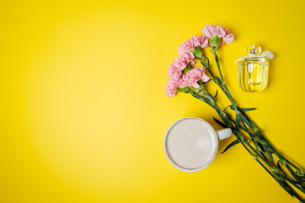 Xícara com café e espíritos de flores de cravo rosa na mesa amarela vista de cima espaço plano para texto