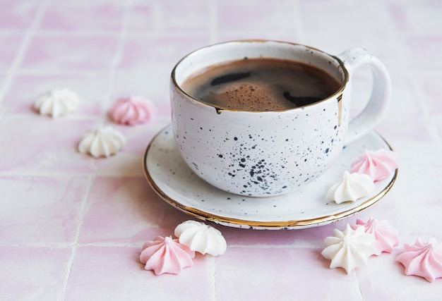 Xícara com café e pequenos merengues sobre fundo de azulejos