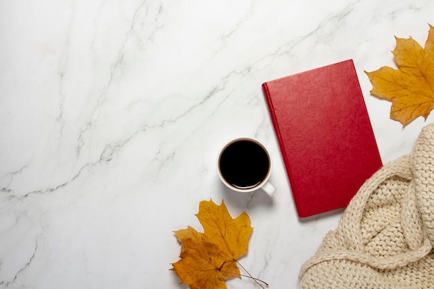 Xícara com café ou chá, folhas amarelas de outono e um livro sobre uma mesa de mármore