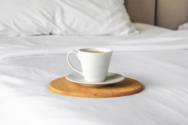 Xícara de café acabado de fazer fica na bandeja de madeira na cama branca limpa Conceito de bom dia