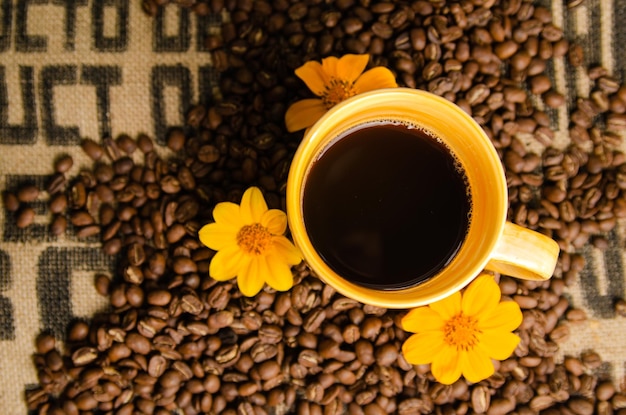 xícara de café amarela com grãos de café na mesa com fundo natural