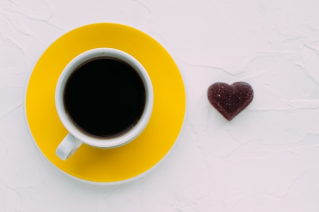 Xícara de café amarela e coração em um fundo branco. minimalismo. fechar-se