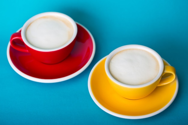 Xícara de café amarela e vermelha linda com cappuccino em fundo azul