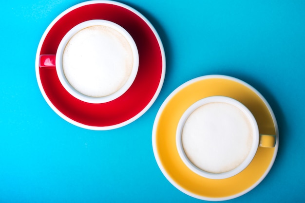 Xícara de café amarela e vermelha linda com cappuccino em fundo azul
