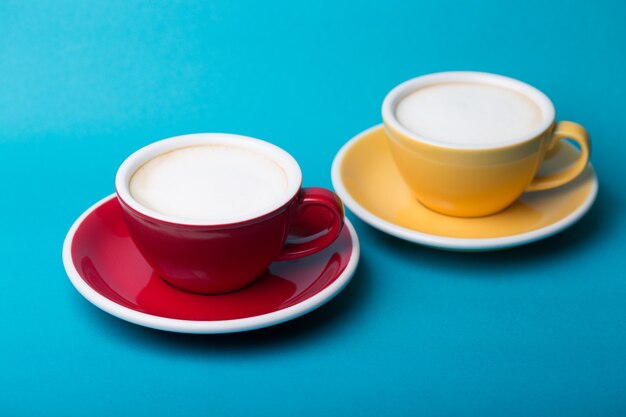 Xícara de café amarela e vermelha linda com cappuccino em fundo azul