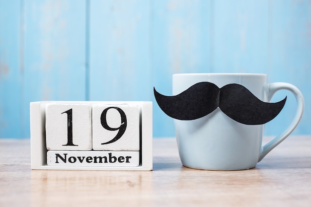 Xícara de café azul, bigode preto e calendário de 19 de novembro. . pai, dia internacional dos homens, conscientização sobre o câncer de próstata