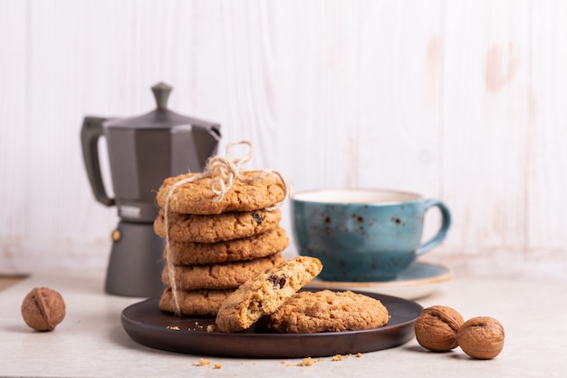 Xícara de café, biscoitos de aveia, cafeteira em fundo branco de madeira.