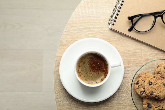 Xícara de café, biscoitos, notebook e óculos na mesa de madeira