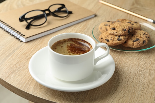 Xícara de café, biscoitos, notebook e óculos na mesa de madeira