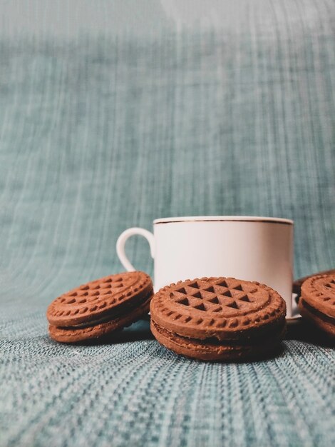 Xícara de café branca e biscoitos redondos marrons em um fundo azul