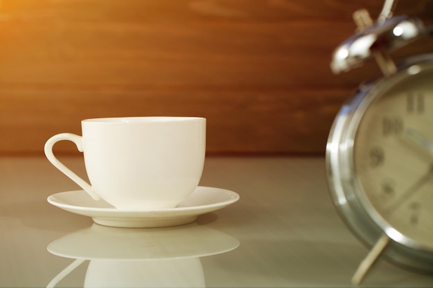 Xícara de café branca e despertador na mesa