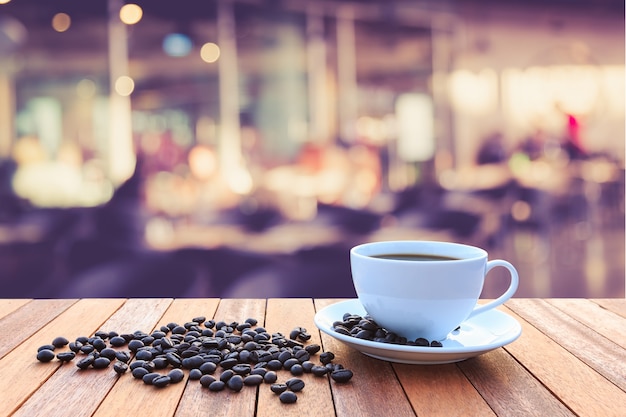 Xícara de café branca e grãos de café na mesa de madeira