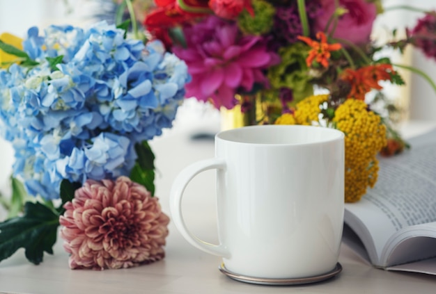 Xícara de café branca entre flores em uma mesa