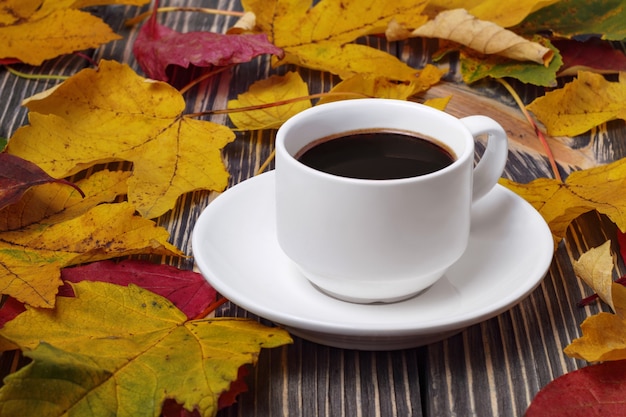 Xícara de café branca na mesa de madeira e folhas amarelas de outono ao redor.