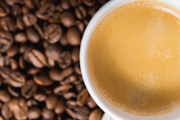 Xícara de café branca pequena com creme de café expresso em fundo de feijão torrado Foco seletivo Closeup