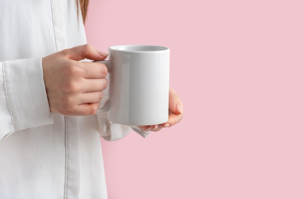 Xícara de café branco de maquete ou caneca em mãos femininas rosa