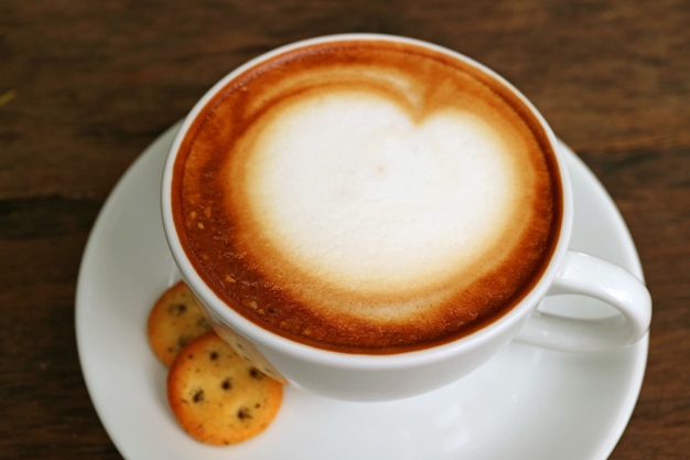 Xícara de café cappuccino com espuma de leite fofo branco em cima da mesa de madeira