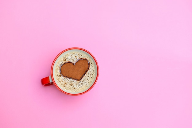 Xícara de café cappuccino com forma de coração no fundo rosa suave. Bom dia conceito Imagem com espaço para cópia, vista superior