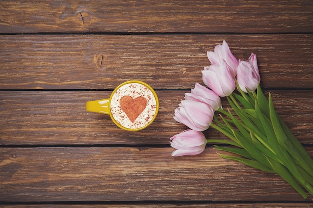 Xícara de café cappuccino com tulipas da primavera na madeira