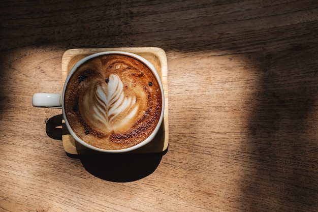 Xícara de café com arte de latte de forma de coração na mesa de madeira