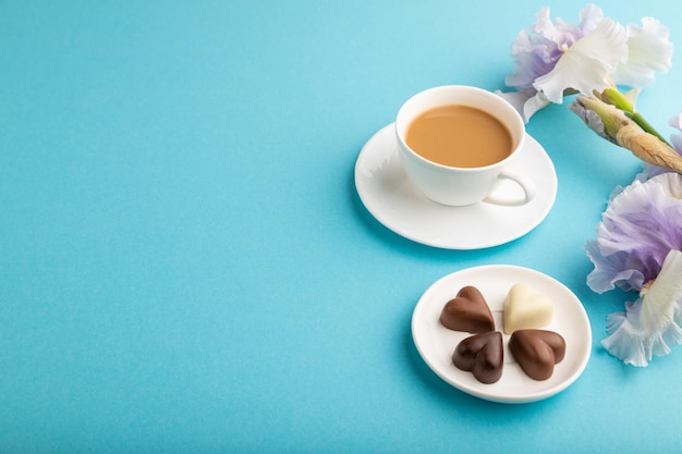 Xícara de café com bombons de chocolate e flores de íris lilás no espaço de cópia de vista lateral de fundo pastel azul