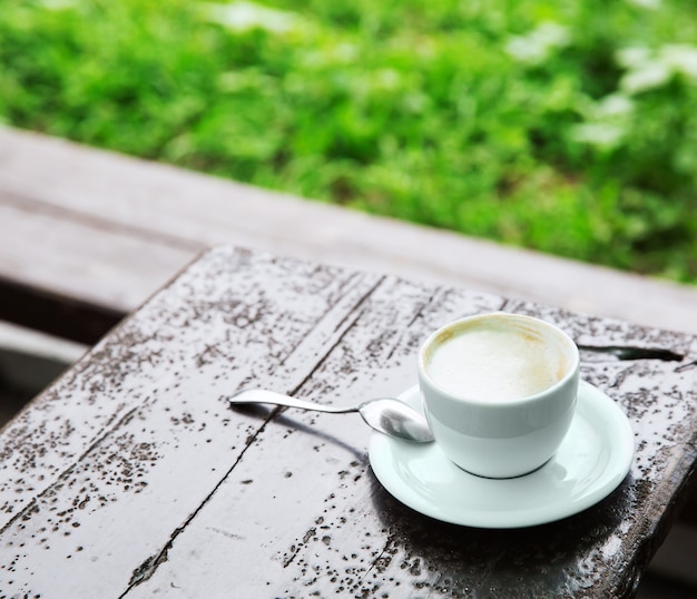 Xícara de café com cappuccino de café em pé sobre uma mesa de madeira no fundo da grama