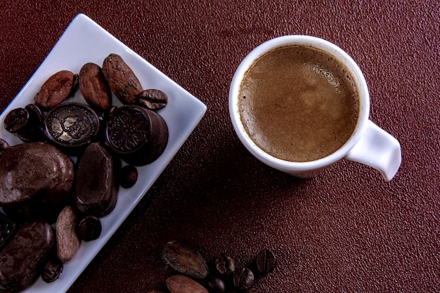 Xícara de café com chocolates fotografados em fundo pintado de marrom