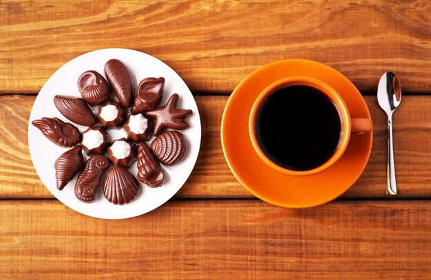 Foto xícara de café com colher e bombons de chocolate na mesa de madeira. ponto de vista superior.