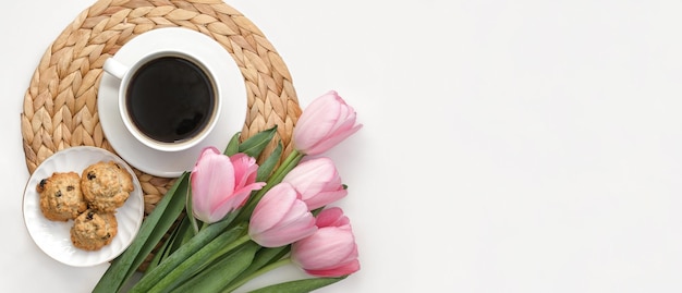 Xícara de café com flores de tulipas cor de rosa fundo branco café da manhã na bandeja de vime vista superior