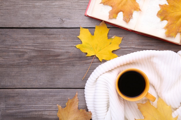 Xícara de café com folhas de outono e livro velho em fundo de madeira