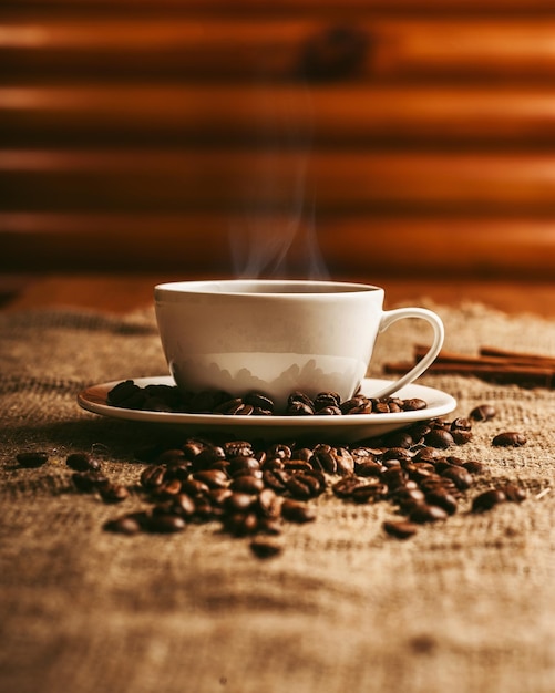 Foto xícara de café com fumaça e grãos de café em serapilheira em fundo de madeira velho