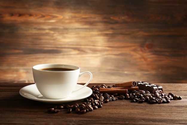 Xícara de café com grãos, chocolate e canela em pau na mesa de madeira