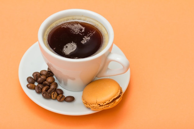 Xícara de café com grãos de café e delicioso bolo de macarons com fundo de cor pêssego