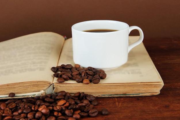 Xícara de café com grãos de café e livro sobre mesa de madeira em fundo marrom